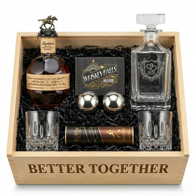 Blanton's Bourbon Date Night gift crate top-down view featuring "BETTER TOGETHER" engraved on front of open wooden crate, Blanton's Original Single Barrel Bourbon 750ml with brass horse stopper, Better Together square crystal decanter with pointed shield crest showing two intertwined hearts, "BETTER TOGETHER" italic text, and elaborate baroque acanthus leaf scrollwork flourishes, two XXL 55mm polished chrome stainless steel whiskey balls, two old-fashioned crystal glasses, and Turin chocolates.