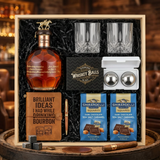Blanton's Gold Edition Single Barrel Bourbon gift crate with gold horse stopper, crystal-cut old fashioned glasses, faux-leather bourbon journal and pen set, premium XXL stainless steel whiskey balls, and two Ghirardelli Dark Chocolate Sea Salt Caramel bags on rustic aged oak surface with warm amber bourbon bar lighting and moody bokeh