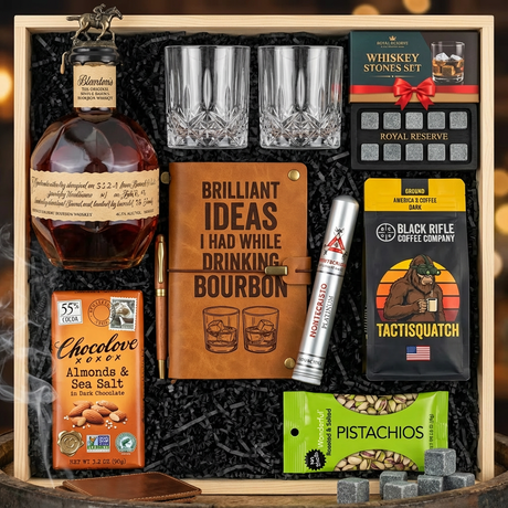 Blanton's Original Single Barrel Bourbon Top Shelf gift crate with bronze horse stopper, crystal-cut old fashioned glasses, Royal Reserve whiskey stones set, bourbon journal, Montecristo Platinum cigar, Black Rifle Coffee, Chocolove chocolate, and Wonderful Pistachios on rustic aged oak surface with warm amber bourbon bar lighting and moody bokeh
