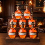 Blanton's Straight From The Barrel Single Barrel Bourbon complete 8-bottle collector's set with bronze horse and jockey stoppers and copper neck bands arranged in pyramid display on tiered dark walnut wooden platform with warm amber bourbon library lighting and sophisticated whiskey lounge ambiance