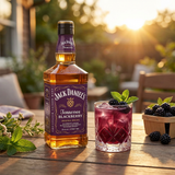 Jack Daniel's Tennessee Blackberry liqueur bottle with distinctive purple label displayed on rustic wood with blackberry cocktail garnish and warm summer patio lighting