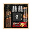 Johnnie Walker Black Label 12 Year Scotch Gift Crate featuring a 750ml bottle, two crystal cut whiskey glasses, Original Whiskey Stones set, Walker's Shortbread Fingers, and Turin Johnnie Walker Bittersweet Chocolates tube, arranged in a light wooden gift box with black crinkle paper