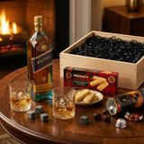 Lifestyle scene of Johnnie Walker Blue Label Scotch gift set being enjoyed on an elegant dark wood table with crystal glasses filled with scotch, whiskey stones, Walker's Shortbread Fingers, and Turin chocolates, with the wooden gift crate in the background