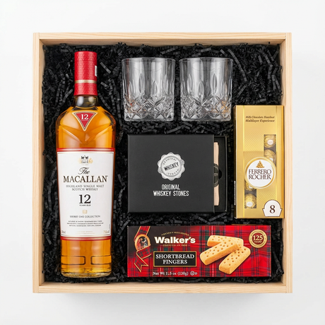 The Macallan 12 Year Sherry Oak Single Malt Scotch gift crate, crystal-cut old fashioned glasses, premium whiskey stones gift set, Ferrero Rocher chocolates, and Walker's shortbread fingers in black crinkle paper on white background