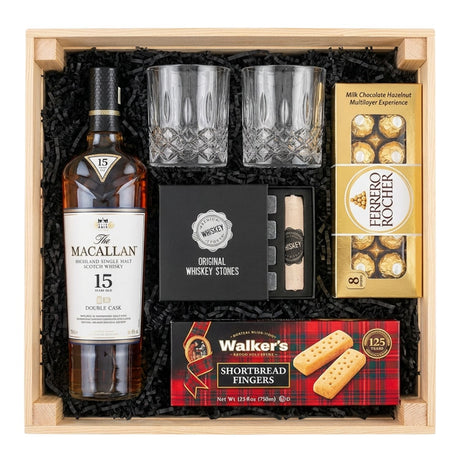 The Macallan 15 Year Old Double Cask Single Malt Scotch gift crate with crystal-cut old fashioned glasses, premium whiskey stones gift set, Ferrero Rocher chocolates, and Walker's shortbread fingers in black crinkle paper on white background