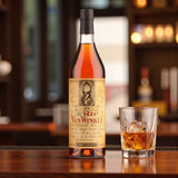 Collector’s Old Rip Van Winkle 10 Year Bourbon bottle on wooden bar beside glass of bourbon with ice and warm bar lighting – Rare Bourbon Shop lifestyle photo