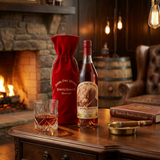 Pappy Van Winkle's Family Reserve 20 Year Old Kentucky Straight Bourbon Whiskey lifestyle scene featuring bottle with red wax top and vintage sepia portrait label alongside red velvet drawstring bag with gold embroidery, displayed with crystal bourbon glass on rich dark wood surface in luxurious bourbon den setting with warm ambient lighting.